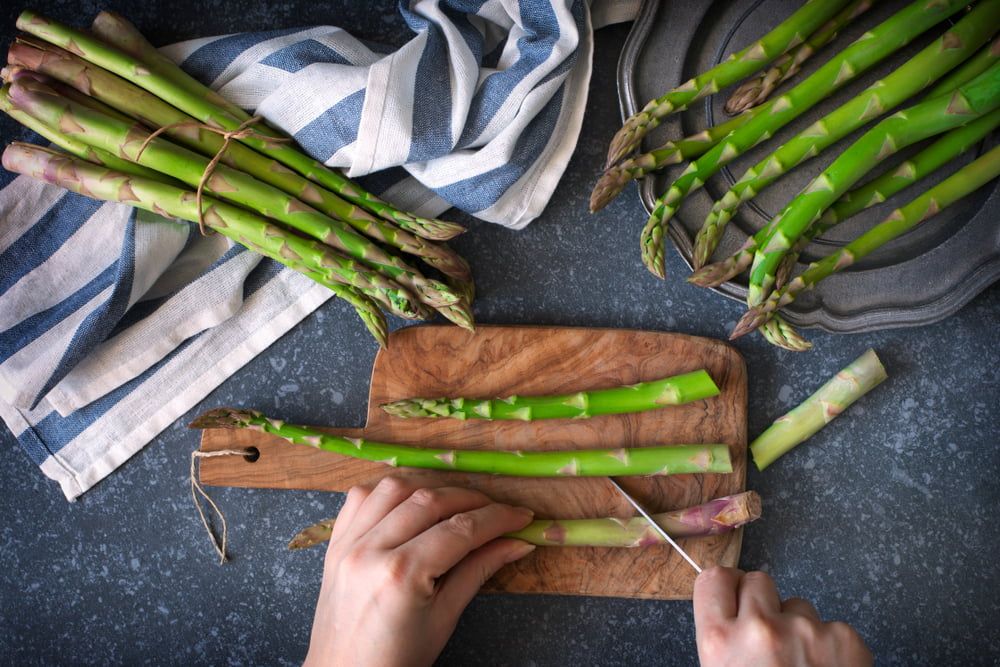 Hands cutting asparagus on chopping board