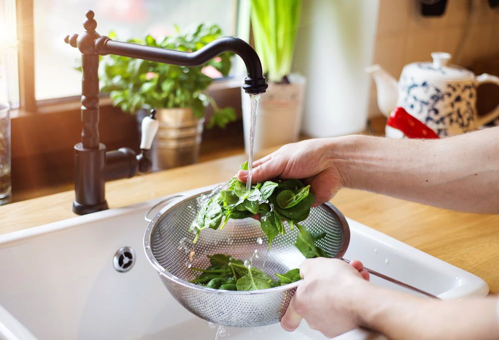 Hands washing spinach in colander